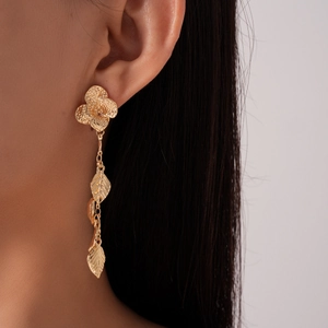 Close-up of golden metallic floral and leaf tassel earrings worn by a female model