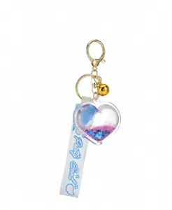 Detail view of heart-shaped quicksand keychain with golden bell and blue ribbon strap