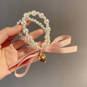 Detail of double-layer pearl bracelet with pink satin bow and golden heart charm
