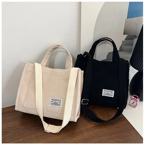 Detail of beige and black corduroy tote bags with adjustable straps on a wooden table