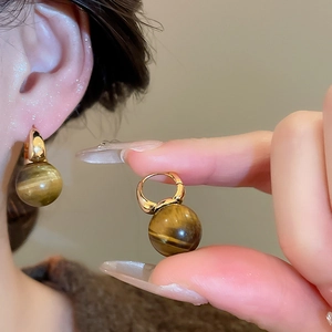 Detail of tiger eye stone earrings with golden heart and floral accents worn by a model
