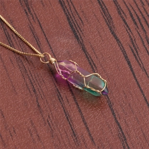 Macro detail of hand-wrapped gradient crystal pendant with golden wire on wood surface