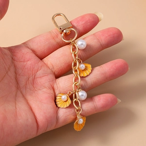 Close-up of golden keychain with starfish shell charms and white pearls held in hand
