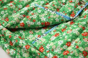 Detailed close-up of green floral quilted cotton jacket with blue contrast piping detail
