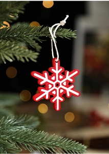 Red wooden snowflake ornament hanging on a green Christmas tree with warm bokeh lights