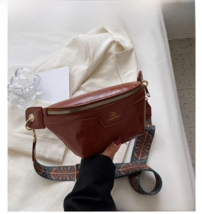 Close-up of brown faux leather chest bag with golden DM logo and geometric woven strap