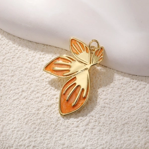 Golden leaf pendant with orange enamel wing design on a minimalist white texture base