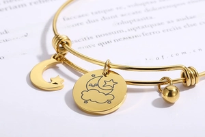 Macro shot of gold adjustable bangle with moon, star charms and laser engraved pendants