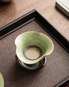 Macro shot of green speckled ceramic tea strainer with gold rim and metal filter mesh