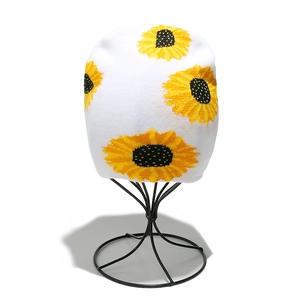 Detailed knit texture of white beanie featuring a vibrant yellow sunflower floral pattern