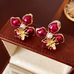 Elegante goldene Bienen- und rote Blumenohrringe mit Perlen auf braunem Lederetui
