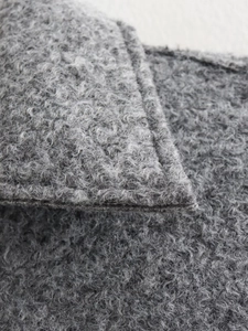 Close-up of grey curly teddy faux fur fabric texture with precise stitched edges