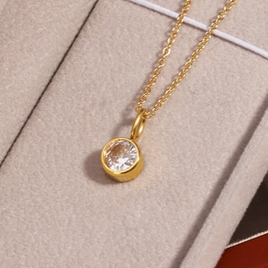Close-up of a gold birthstone necklace with a round clear crystal in a beige velvet box