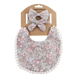 Detailed view of floral baby bib with pom-pom trim and two matching bow headbands