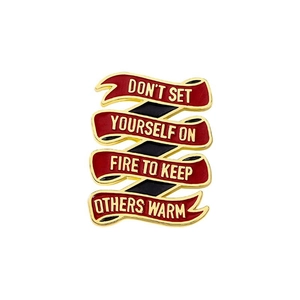 Detail of red enamel ribbon brooch with text: Don't set yourself on fire to keep others warm