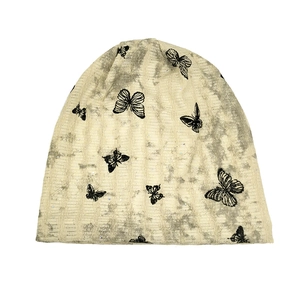 Macro detail of beige knit beanie with black butterfly patterns and subtle glitter texture