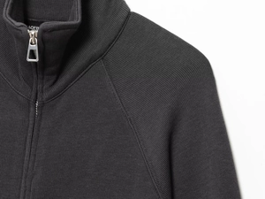 Detailed close-up of a black high-density knit cardigan featuring a silver metal zipper