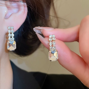 Detail of square crystal drop earrings with silver finish worn on the ear model