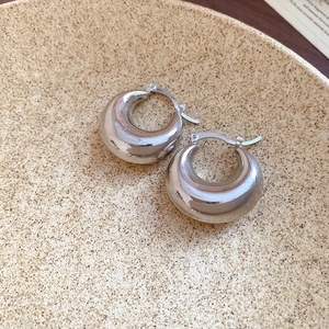 Close-up of thick silver C-shaped hoop earrings on a textured ceramic display plate