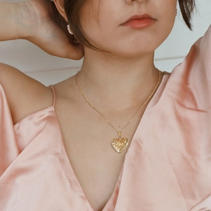 Detail of a gold heart-shaped locket pendant with intricate filigree on a neck chain