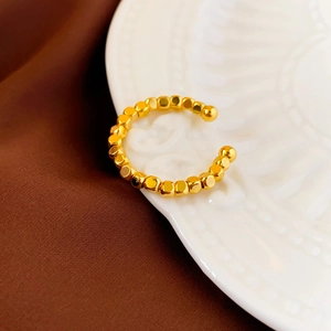 Macro shot of gold-plated beaded geometric open ring on white embossed ceramic plate