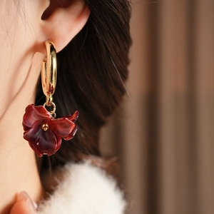 Detailed close-up of dark red petal earrings with gold hoops on model's ear
