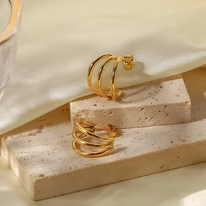 Detailed view of triple-layered 18K gold titanium earrings on white silk and beige stone