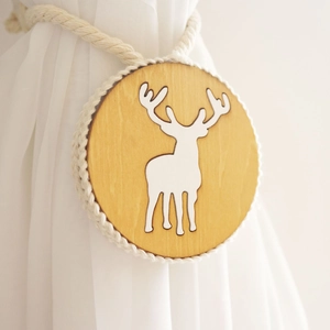 Detail view of wooden curtain tieback with white deer motif and braided cotton rope