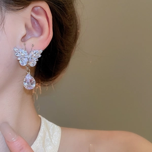 Close-up of silver butterfly earrings with clear zircon crystals and teardrop pendants