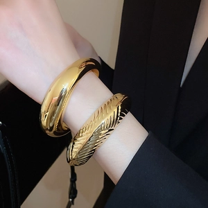 Détail de bracelets ovales dorés avec textures polies et plumes portés par un mannequin