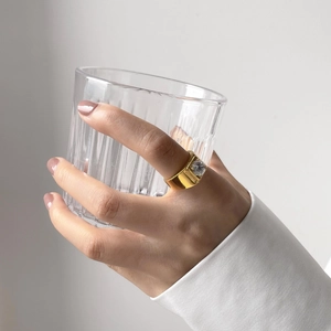 Close-up of golden gear design ring with clear gemstone worn while holding a glass