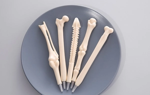 Detailed view of five bone-shaped ballpoint pens on a minimalist grey display tray