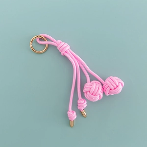 Close-up of pink hand-woven nylon bag charm with golden metal ring and ball knot details