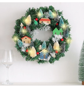 Green Christmas wreath with LED lights, small wooden cabin and colorful sisal trees