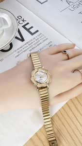 Vintage gold women's watch with flower-shaped case worn on wrist in a cozy cafe setting
