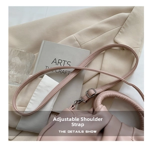 Detail of adjustable strap on a pink pleated cloud bag atop books and a blazer