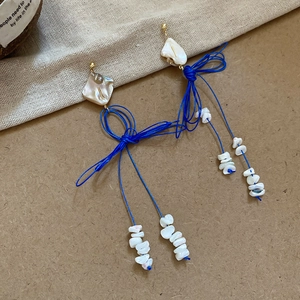 Détail de boucles d'oreilles à pompons bleus avec breloques en coquillage et doré
