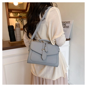 Chic grey leather crossbody bag shown in a stylish cafe setting with adjustable strap