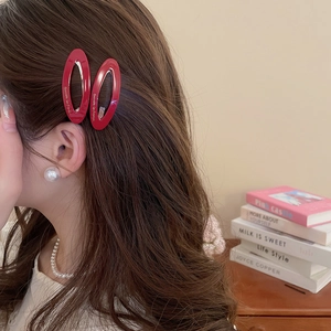 Close-up of elegant red oval hair clips with gold lettering on wavy brown hair