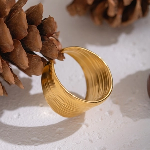 Close-up of golden brushed stainless steel open ring resting on natural pine cone