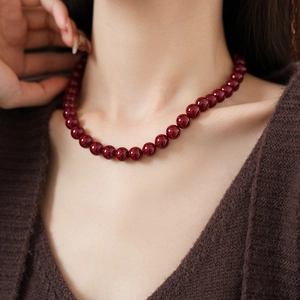 Close-up of red beaded necklace with glossy round beads worn by a model in soft lighting