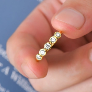 Macro shot of gold five-stone ring with bezel-set round clear moissanite on finger