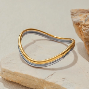 Dettaglio di un bracciale rigido ondulato bicolore oro e argento in acciaio su pietra
