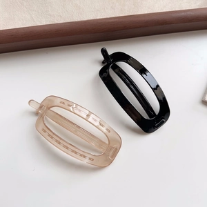 Detailed view of minimalist oval hair clips in glossy black and clear champagne finishes