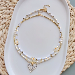 Detail of layered bohemian necklace featuring white daisy flowers and heart pendant