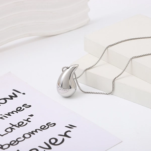 Minimalist silver teardrop pendant necklace on sleek snake chain with a white stone background