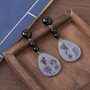 Detail of fan-shaped pearl tassel earrings with engraved Chinese characters on a wooden frame