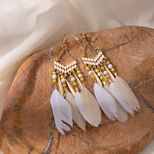 Close-up of bohemian tassel earrings with yellow beads and white feathers on stone
