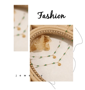 Detail of double-layer gold necklace with green beads and shell pendant on textured paper