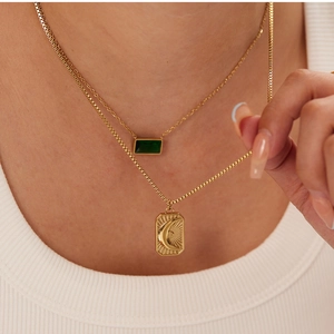 Detail of layered gold stainless steel necklace with green stone and sun moon pendants